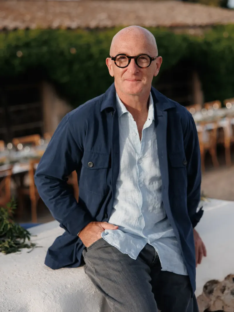 Errol Damelin in Menorca — navy jacket over white linen, outdoor dining.